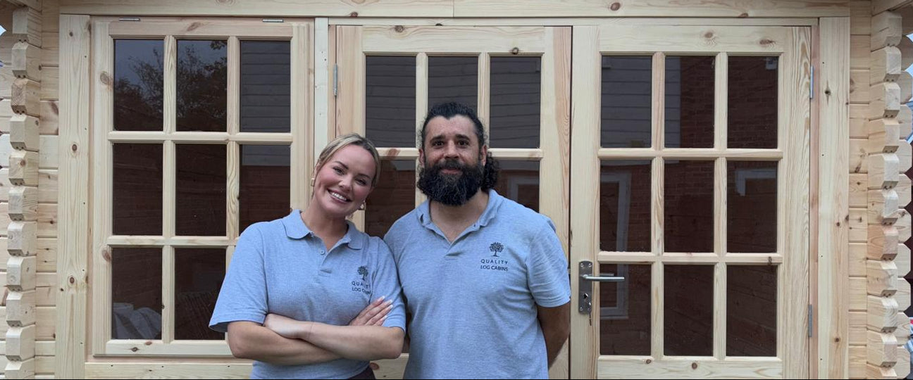 Two people standing in front of a wooden cabin.